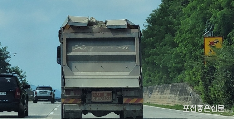 허술한 덮개 사이로 보이는 흙 위의 돌이 곧 떨어질 것 같은 상황에도 화물차량은 도로 위를 질주하고 있다.